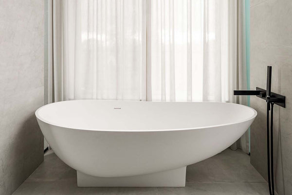 eggshell white stone bathtub set in modern bathroom with concrete walls